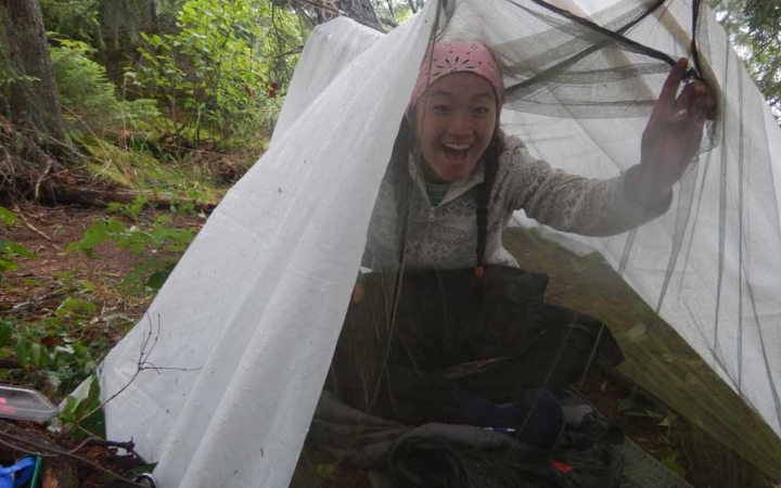 a person smiles from under a shelter in a wooded area